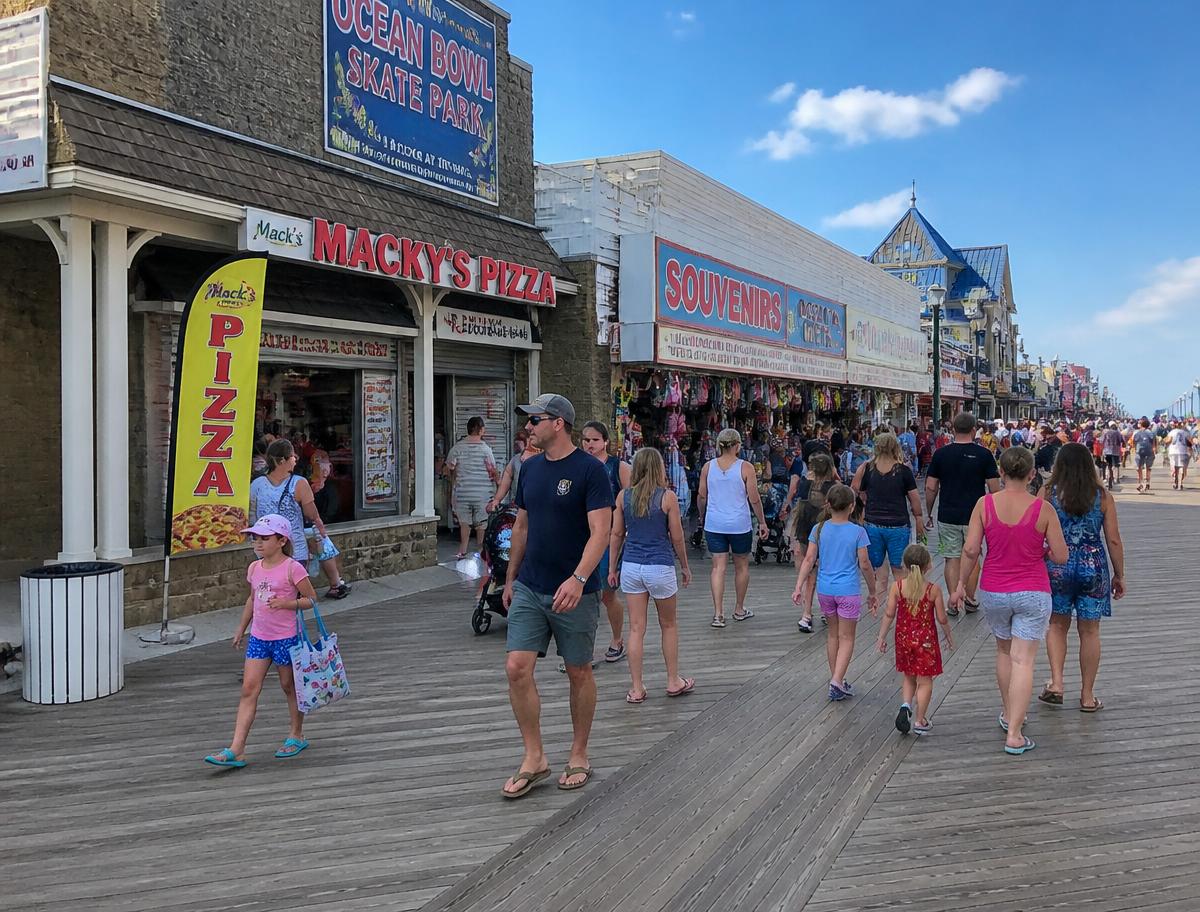 Families walking past pizza and souvenir shops on a busy seaside boardwalk