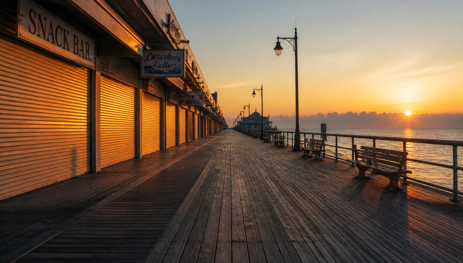 Quiet off-season boardwalk at golden hour with shuttered shops and empty benches